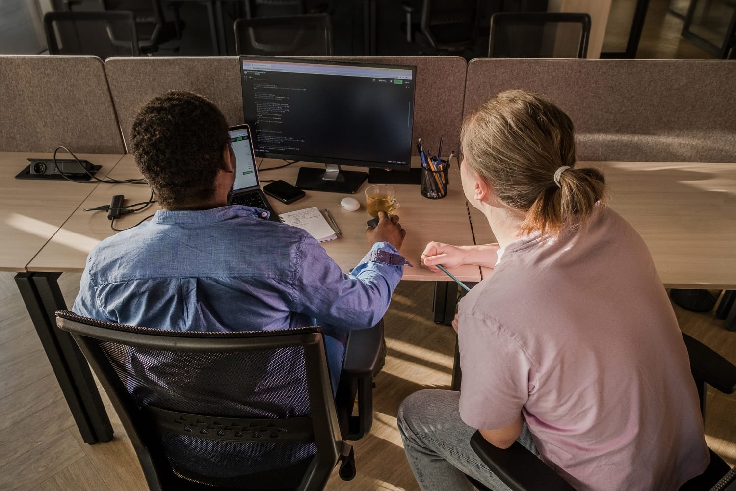 Two IT professionals collaborating on code at a shared workspace, representing innovation and cybersecurity expertise.