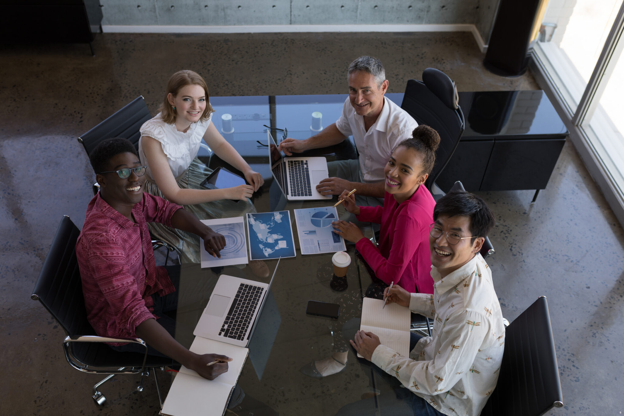 Diverse team of professionals collaborating at a conference table with laptops and data charts.